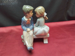 A Cute NAO Figure of A Girl & A Boy on 5he Bench. W.13 H.17 Cm.