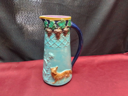 An Embossed Majolica Jug with Moulded Decoration of dogs and Grapes in Green. W.13 H.22 Cm.