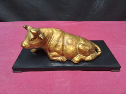 A statue of a golden bull laying down on a base 8x18 Cm..