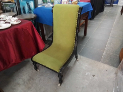 A vintage Victorian-style slipper chair featuring green upholstery, an ebonized wooden frame, and brass studded details