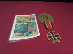 A German 1939 Iron Cross and a ribbon  and mounted on a green backing with an oak leaf insignia.