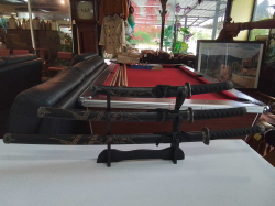 A 3 piece Japanese Katana Samurai sword set featuring dragon engravings on the black scabbards and a matching black display stand.