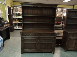 An antique 20th-century dark oak dresser features distinctive linenfold carved panels and a scalloped cornice. W.130 D.47 H.185 Cm.