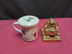 A handpainted chinese lidded cup. H.9 Cm. and Chinese gold colored guardian dog sat on coins on its own base. W.8 D.9 H.8 Cm.