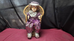A vintage clown doll with a porcelain head sitting on a small wicker chair 40 cm high