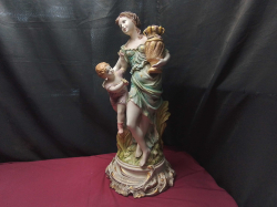 A porcelain Capodimonte ornate with a cherubic child and Lady carrying a harvest urn 
H65cm. W26cm.
