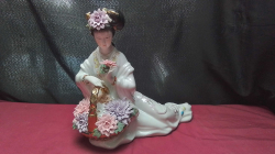 An Asian porcelain figurine of a seated. Geisha/Guanyin holding a floral basket with gold trim.